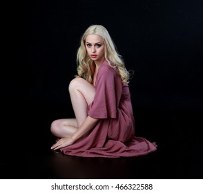 Beautiful blonde haired woman wearing a long flowing purple dress, kneeling on the ground.  isolated on a black background.