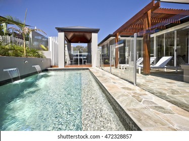 Modern swimming pool side with glass cover and wooden patio, the light blue water can be seen deeply beside the poolside with a wooden pillars and beams under blue sky