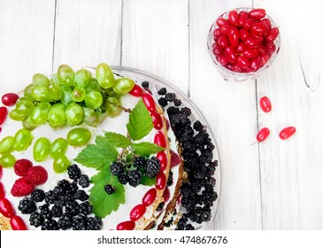 Kuchen mit Weißwein, Früchten (Trauben) und Beeren (Himbeeren, Brombeeren, Kornelkirsche) als Dekoration oben drauf. Kristallglas daneben mit Hartriegelbeeren (Kornblume). Hausgemachter frischer Kuchen. Ansicht von oben.