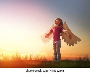 少女は屋外で遊ぶ。夕焼け空の背景の子。鳥の羽を持つ子供は空を飛ぶことを夢見ています。