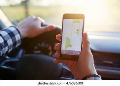 Hombre en el auto y sosteniendo un teléfono móvil negro con navegación gps de mapa, tonificado al atardecer.