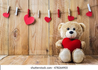 Ein Foto des Teddybären, der ein herzförmiges Kissen auf einem Plankenholzbrett mit Holzbretthintergrund hält
