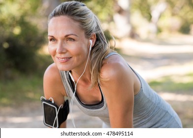 Retrato de mujer madura atlética descansando después de trotar. Hermosa mujer rubia senior corriendo en el parque en un día soleado. Corredora escuchando música mientras trota.