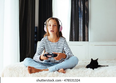 10 Jahre altes jugendliches Mädchen, das Spielekonsole hält und am Morgen auf einem Sofa zu Hause spielt