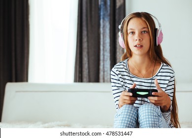 10 Jahre altes Mädchen vor dem Teenager, das eine Spielkonsole hält und morgens zu Hause auf einem Sofa spielt