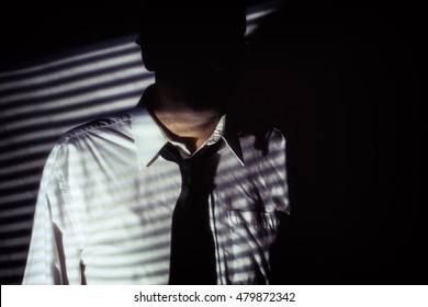 Interrogador do Homem Sombra Sem Rosto. Homem misterioso e anônimo com o rosto escondido nas sombras das persianas, vestindo camisa branca e gravata preta. Filmado no estilo de filme noir.