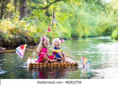 Two children on wooden raft catching fish with a colorful net in a river and playing with water on hot summer day. Outdoor fun and adventure for kids. Boy and girl in toy boat. Sailor role game.