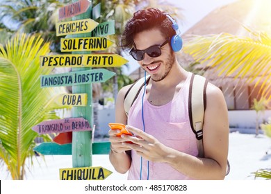 Junger Reisender auf der Insel Holbox (Mexiko) mit einem Schild, das auf nahegelegene Städte und lokale Spezialitäten hinweist.
