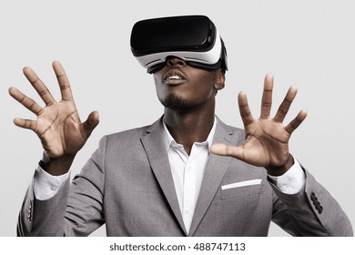 Technologie-, Spiele-, Unterhaltungs- und Personenkonzept. Afrikanischer Mann, der formellen Anzug und Virtual-Reality-Headset oder 3D-Brille trägt, Videospiel spielt, mit seinen Händen gestikuliert und etwas fängt