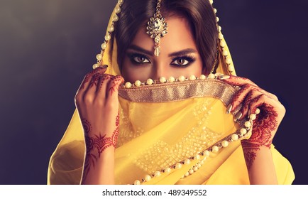 Schönes indisches Mädchen. Junges hinduistisches Frauenmodell mit Tätowierungsmehndi und Kundanschmuck. Gelber Saree der traditionellen indischen Tracht. Indische oder muslimische Frau bedeckt ihr Gesicht.