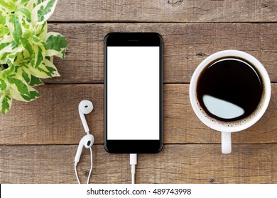 木製のテーブルにスマートフォンの白い画面、モックアップのモダンなスマートフォンのジェットブラックカラー