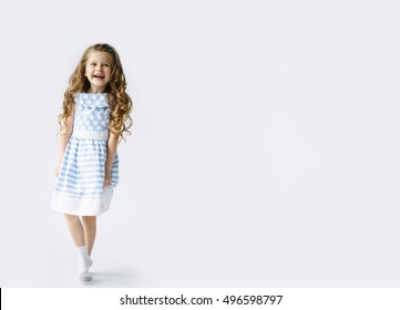 Funny kid in blue and white dress jumping and laughing on light blank background. Little pretty girl isolated on white background. Copy space for text. Sale, holidays, birthday party concept.
