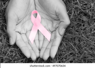 女性の手は、ピンクのリボンの意識乳がんがん意識ループの象徴的なロゴを上げるサポートを保持し、白黒の背景に住む人々の生活を助けます