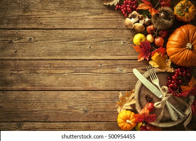 古い木製のテーブルにビンテージの場所を設定して、落ち葉や果物から秋の背景。感謝祭の日のコンセプト