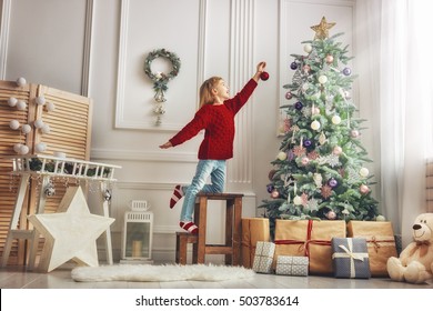 Merry Christmas and Happy Holidays! Cute little child girl is decorating the Christmas tree indoors.