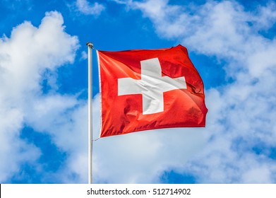 Klassieke weergave van de nationale vlag van Zwitserland zwaaiend in de wind tegen blauwe lucht en wolken op een zonnige dag in de zomer op 1 augustus, de nationale feestdag van de Zwitserse Bondsstaat