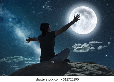 mujer sentada y levantando los brazos a la luz de la luna