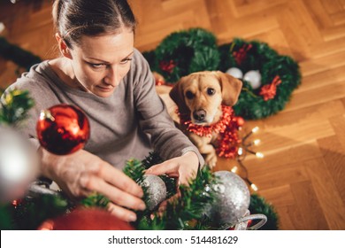 Dona amb un jersei marró decorant l'arbre de Nadal i un petit gos groc assegut al seu costat