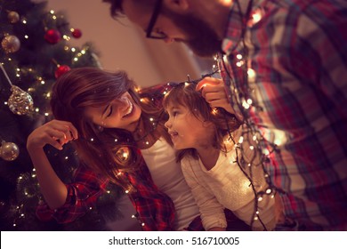 Beautiful young family enjoying their holiday time together, decorating Christmas tree, arranging the christmas lights and having fun