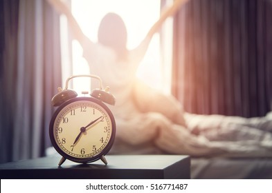Nahaufnahmewecker, der einen guten Tag mit der glücklichen Frau des Hintergrunds im Bett nach dem Aufwachen, Sonnenlicht am Morgen streckt.