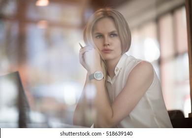 Durchdachtes Konzept. Frau, die an einem Computer in einem Café arbeitet, während sie durch das Fensterglas schaut.