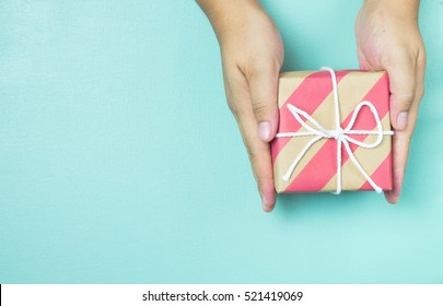 Manos sosteniendo una caja de regalo de papel artesanal como regalo para Navidad, año nuevo, día de San Valentín o aniversario sobre fondo azul, vista superior