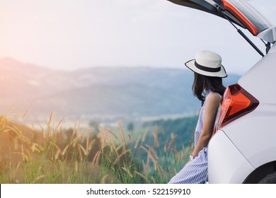 Woman traveler sitting on hatchback car with mountain background in vintage tone