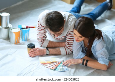Couple choosing paint colour from swatch for new home lying on wooden floor