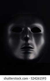 Anonymous black mask protruding from pitch black background. Anonymity concept