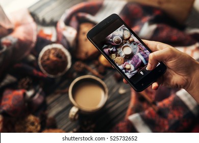 インスタグラム写真ブログワークショップのコンセプト。木製の素朴な背景にスタイリッシュな冬のフラット レイ コーヒー クッキーとスパイスの写真を撮る携帯電話を持っている手。アットホームな雰囲気の秋。