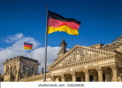 Banderas alemanas ondeando en el viento en el famoso edificio del Reichstag, sede del Parlamento alemán (Deutscher Bundestag), en un día soleado con cielo azul y nubes, distrito central de Berlín Mitte, Alemania