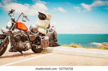 革のジャケットとサングラスを身に着けているバイカーの男は、美しい風景に戻って彼のビンテージ バイクに座っています。