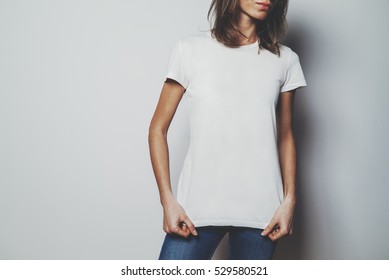 ブルー ジーンズと空白の白い t シャツを着て、ロゴやデザイン、白い t シャツのモックアップ、背景に白い壁を身に着けている若い流行に敏感な女の子