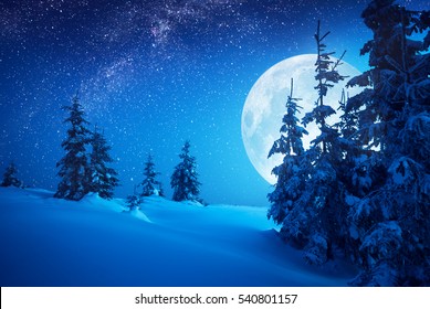 Volle maan stijgt boven de wintervallei bedekt met verse sneeuw. Fantastische melkweg in een sterrenhemel. Kerstnacht.