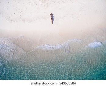 Người phụ nữ trẻ trong bộ bikini nằm ngửa trên bãi cát gần sóng biển xanh. Nhìn từ trên xuống. Đảo Kai, Biển Andaman, Phuket, Thái Lan. Bắn súng trên không.