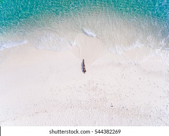 Junge Frau in einem Bikini, der auf dem Rücken auf dem weißen Sand nahe den Wellen des blauen Meeres liegt. Draufsicht. Kai Insel, Andamanensee, Phuket, Thailand. Luftaufnahmen.