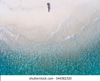 Junge Frau in einem Bikini, der auf dem Rücken auf dem weißen Sand nahe den Wellen des blauen Meeres liegt. Draufsicht. Kai Insel, Andamanensee, Phuket, Thailand. Luftaufnahmen.