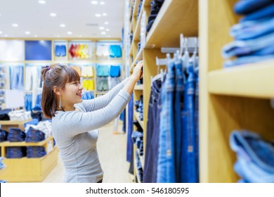 Compradora asiática sonriente eligiendo jeans nuevos en la tienda