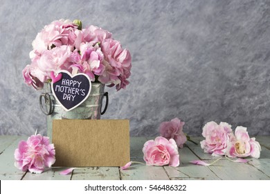 Rosa Nelkenblumen im Zinkeimer mit glücklichem Muttertagsbrief auf Holzherz und leerer brauner Karte