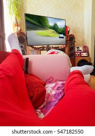 Seorang lelaki sedang berbaring di atas sofa dan menonton filem aksi di TV pintar skrin ratanya. Foto diambil dari sudut pandangan orang pertama.