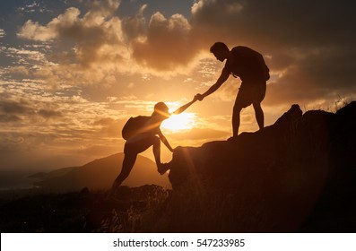 Male and female hikers climbing up mountain cliff and one of them giving helping hand. People helping and, team work concept.