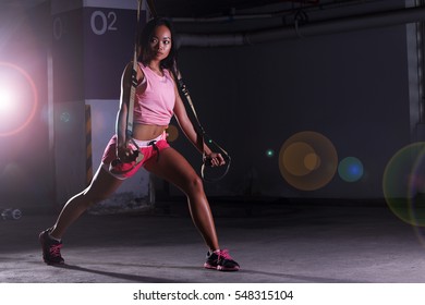 Tan Skin Woman in Fitness pink Suit red short do heavy TRX rope push up ejercicio de entrenamiento en crossfit Garage, iluminación de estudio de sombra oscura, mira a la izquierda, copia espacio para el logotipo de texto