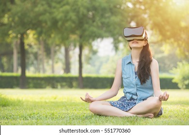 mooie Aziatische vrouw geniet van zen virtual reality zittend op het gras in openluchtpark. VR-headset bril apparaat. natuur buitenshuis achtergrond. mensen en technologie concept