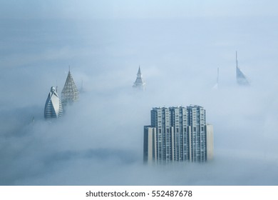 Vista do "Burj Khalifa", o edifício mais alto do mundo, em uma manhã nublada com muita neblina cobrindo a cidade de Dubai. Mostra alguns belos picos de edifícios.