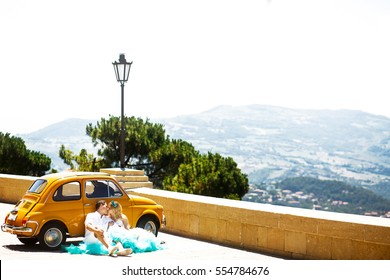 キスをするカップルは、黄色のレトロなフィアット 500 の前に座って、後ろに素晴らしい景色を眺める