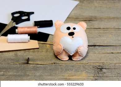 Süßes Kuscheltier Teddybär. Teddybär mit Herz aus Filz. Bastelmaterialien auf Holzhintergrund mit Kopierraum für Text. Einfaches handgemachtes Spielzeug für Valentinstag, Muttertag