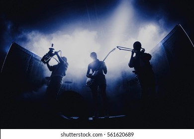 コンサートでのバンドのシルエット。ステージで演奏するサックス、ギター、トロンボーン奏者のグループ。