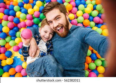 Vrolijke bebaarde vader en zoontje praten selfie bij zwembad met kleurrijke ballen