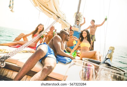 Eine Gruppe von Freunden unterschiedlicher Herkunft feiert ausgelassen auf einem Segelboot mit DJ-Set – Freundschaftskonzept mit jungen Menschen verschiedener Kulturen auf einem Segelboot – Reise-Lifestyle in exklusiver Atmosphäre – Warmer, heller Filter