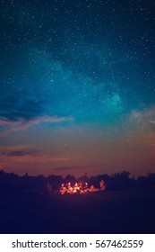 輝く星と雲がたくさんある素晴らしい青い星空の下でのキャンプファイヤー。レクリエーションの野外活動のコンセプトを旅行します。